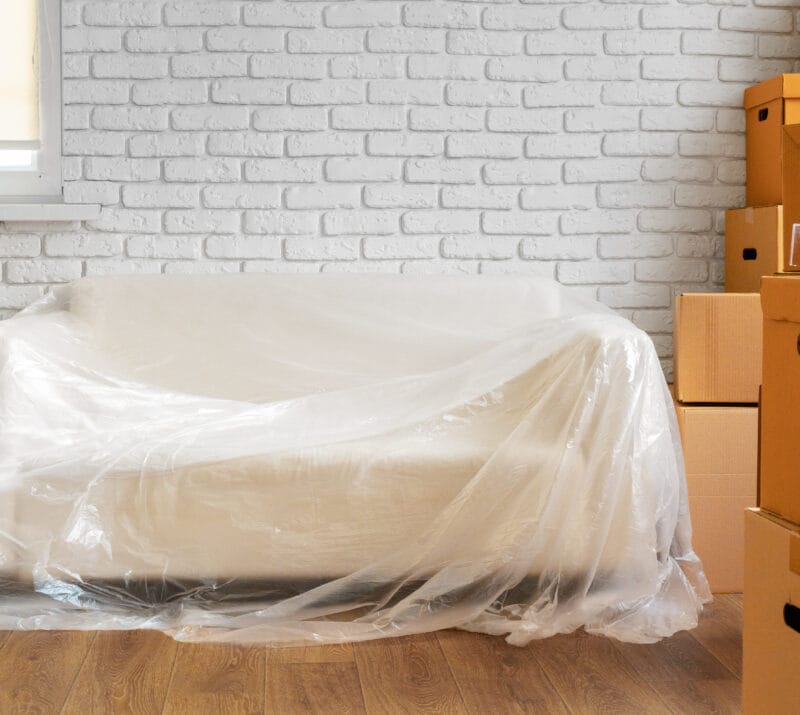 movers in dubai - Packed sofa and stack of cardboard boxes in a room. Moving concept